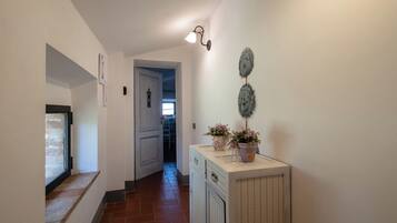 A hallway with a door leading to a room, a small window, and a cabinet with decorative items.
