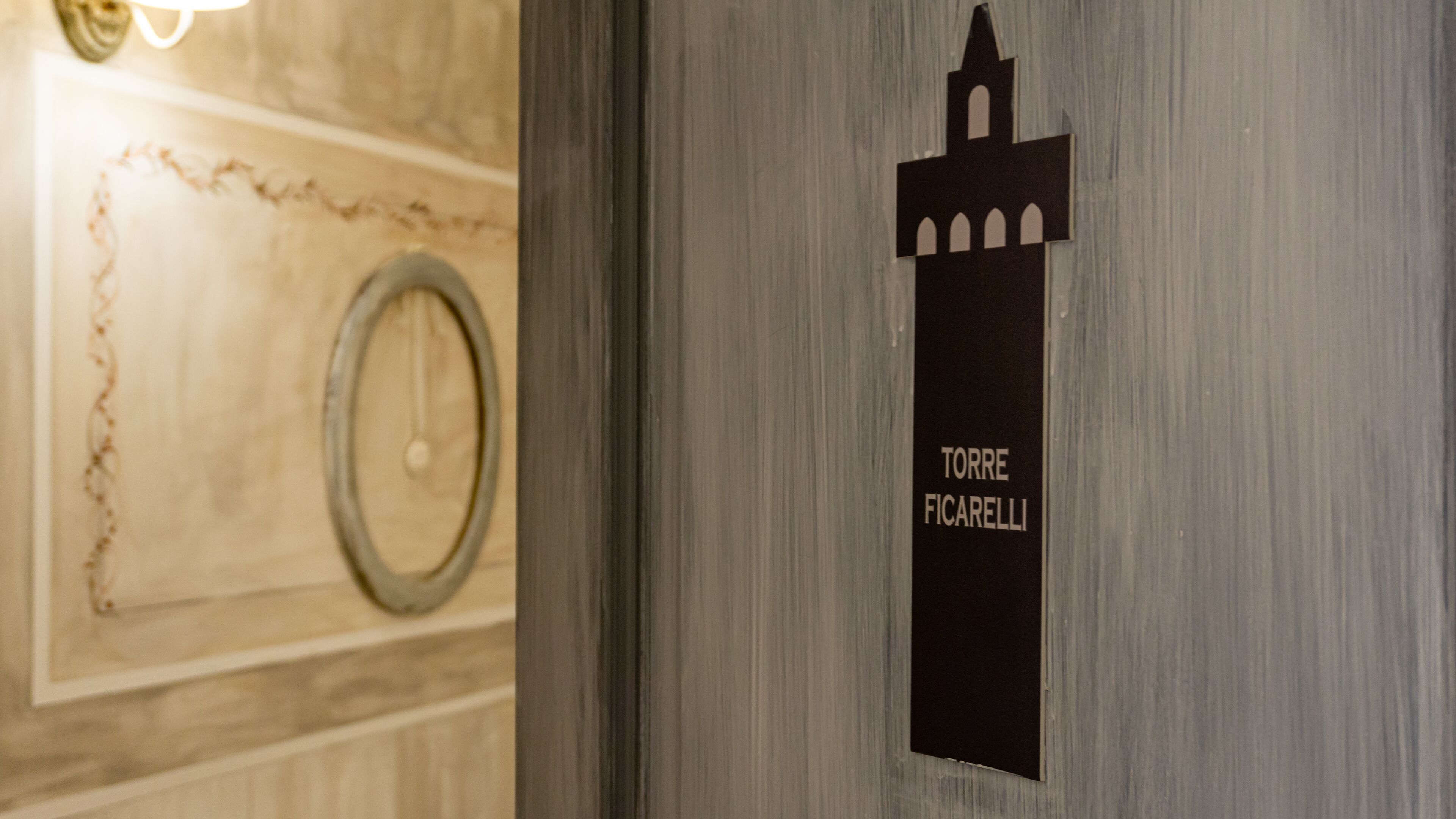A door with a sign reading "TORRE FICARELLI" and a decorative wall with a circular object.