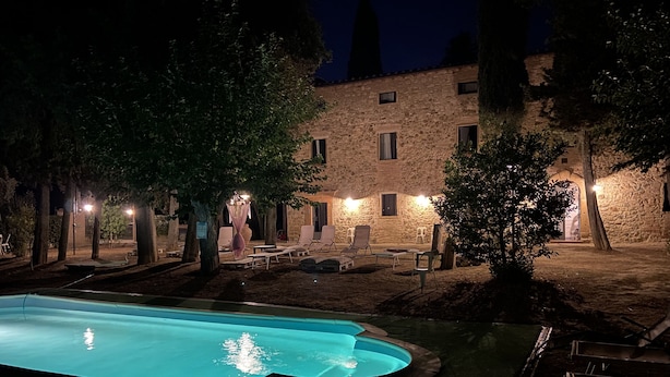 A stone building with a swimming pool, outdoor seating, and trees.