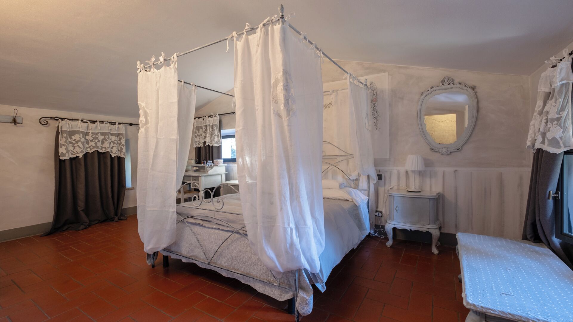 A four-poster canopy bed with a white canopy, a small bedside table, a mirror, and a bench.