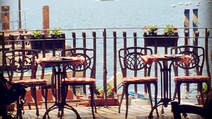 A view from an outdoor seating area with tables and chairs, overlooking a body of water with a boat in the distance. - Hotel Monte Baldo (Limone sul Garda)