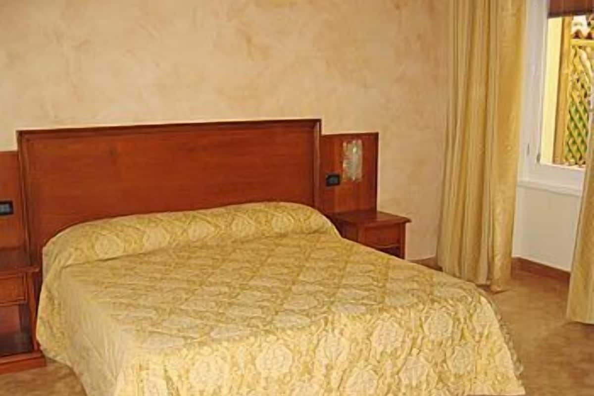 A bed with a quilted cover, a wooden headboard, and a nightstand with a lamp.