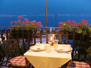 A table set for two with a view of the sea, a railing with flowers, and a chair with a checkered cushion. - Hotel Monte Baldo (Limone sul Garda)