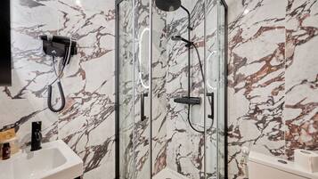 A modern bathroom with a glass-enclosed shower, a white sink, and marble-patterned walls.