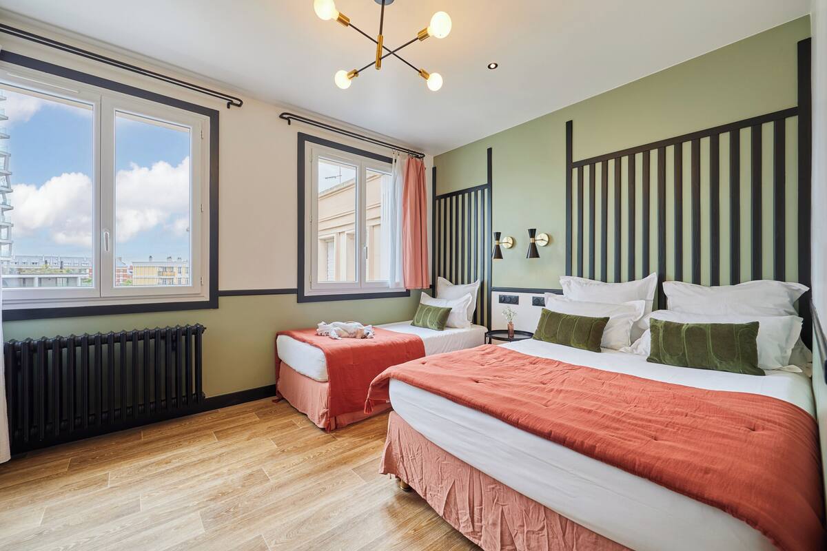 A hotel room with two beds, a radiator, a window with curtains, and a city view.