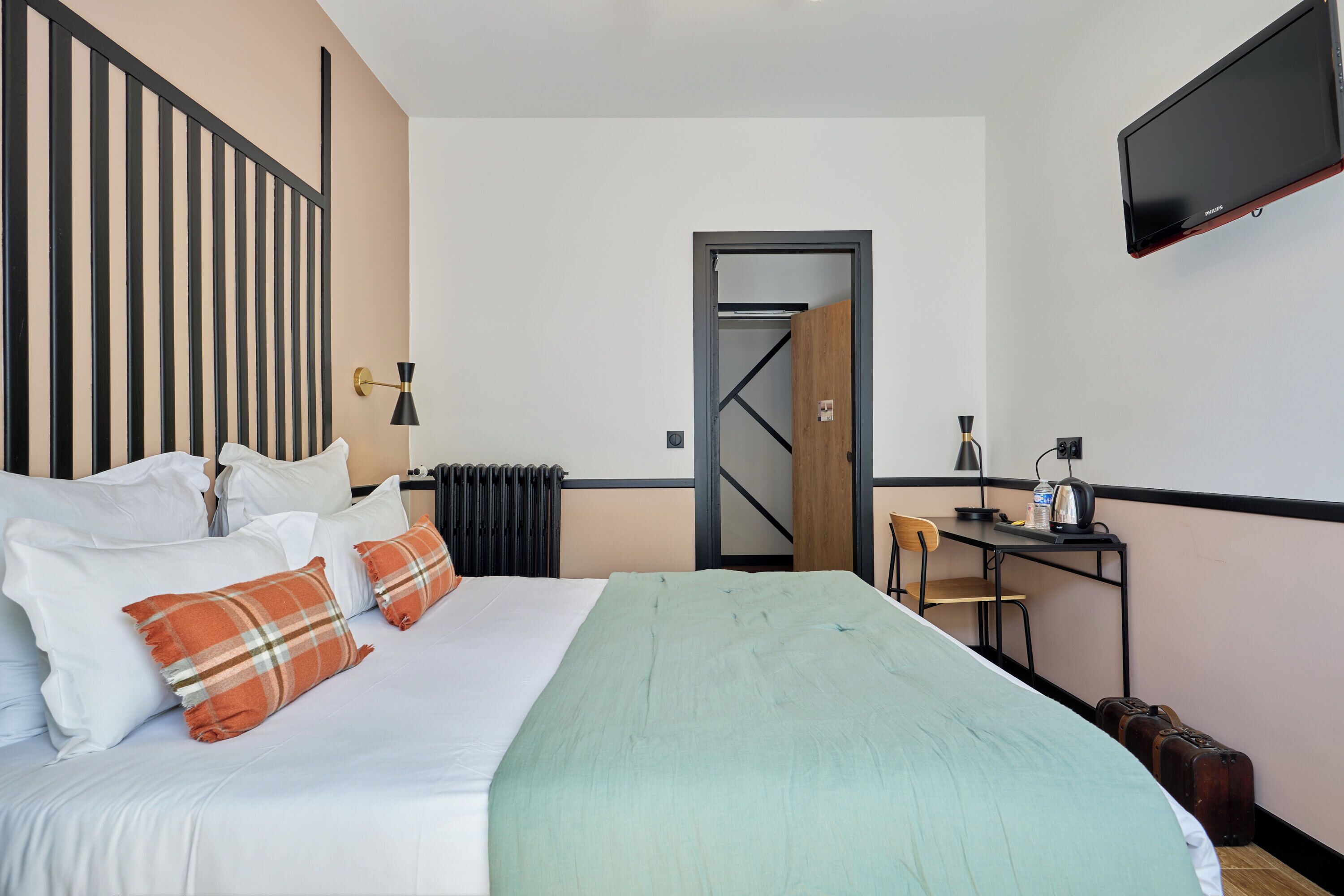 Une chambre d’hôtel équipée d’un lit, d’oreillers, d’un bureau, d’une chaise, d’une télévision et d’un radiateur.