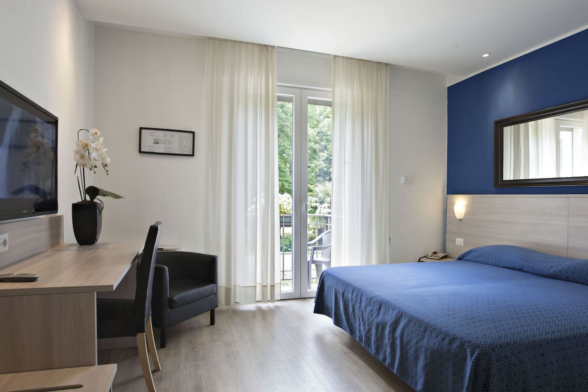 A modern hotel room with a bed, a desk, a chair, and a television.