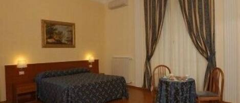 A bedroom with a bed, a table with chairs, a painting on the wall, and curtains.