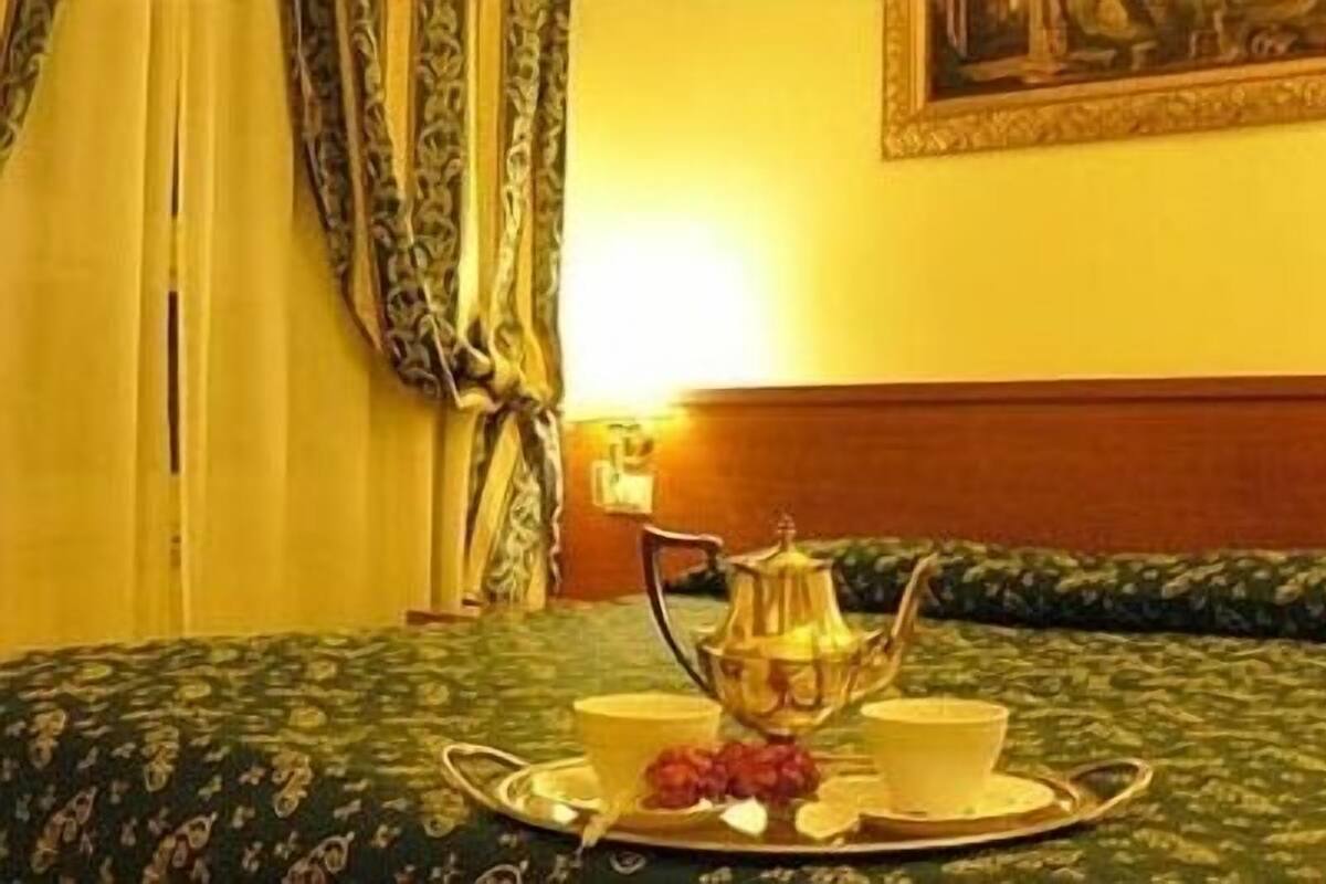 A hotel room with a bed, a tray with a teapot, cups, and grapes, and a painting on the wall.
