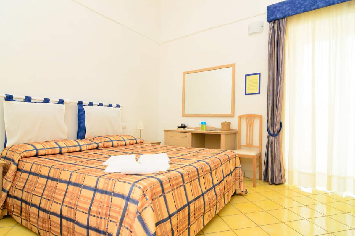 Quarto de hotel com cama, escrivaninha, cadeira, espelho e cortina.