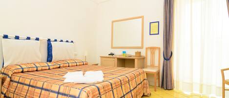 Una habitación de hotel con cama, escritorio, silla, espejo y cortina.
