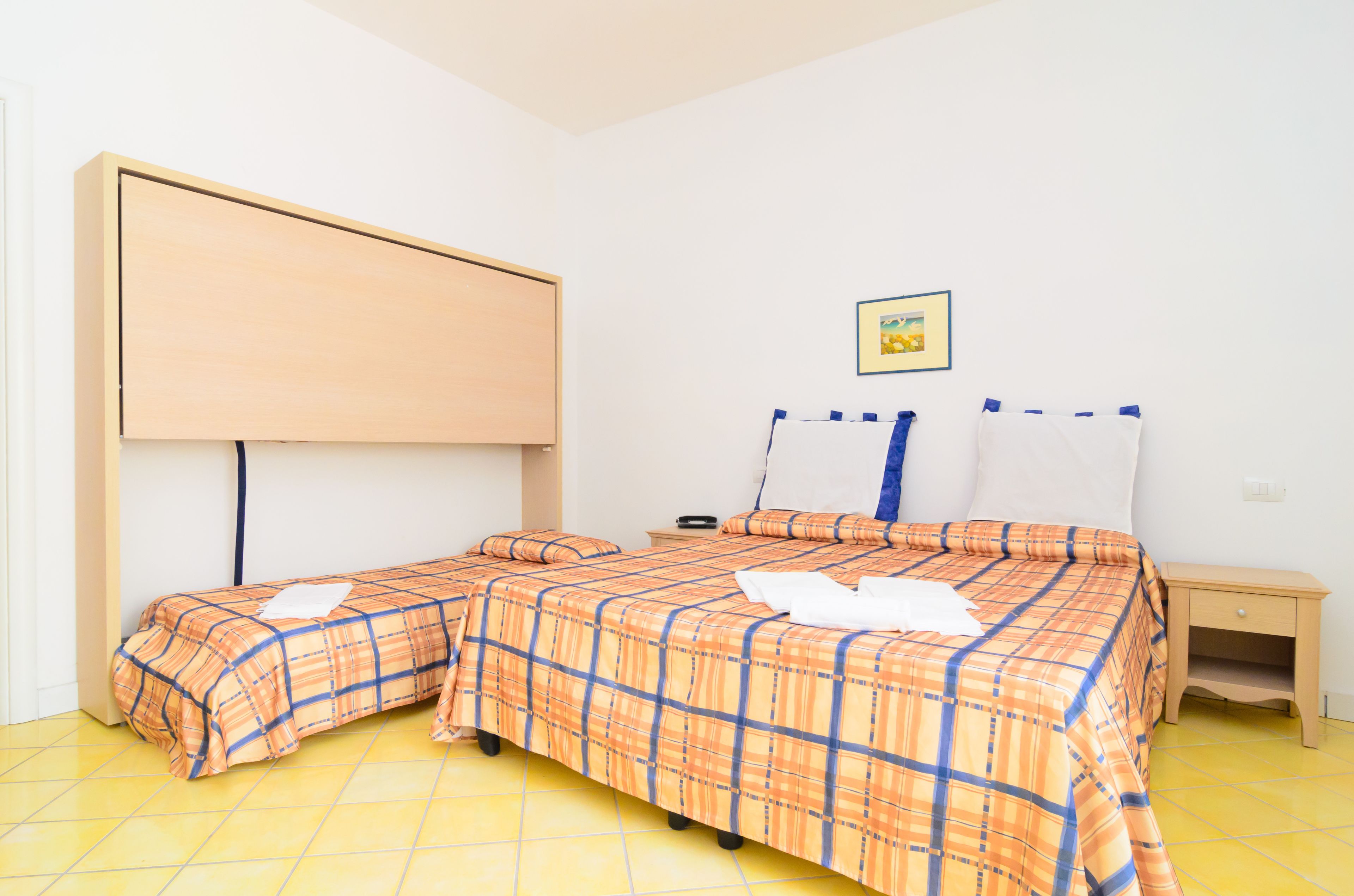 Habitación con dos camas, cabecero de madera, mesita de noche pequeña y un cuadro colgado en la pared.