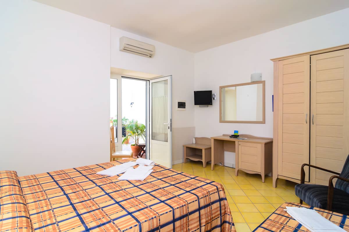Quarto de hotel com uma cama, uma escrivaninha, uma cadeira, um guarda-roupa e uma televisão.