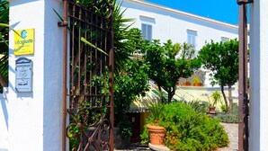 A gated entrance with a metal gate, a stone pathway, and a white building with a sign. - Albergo Villa Giusto (Barano d'Ischia)