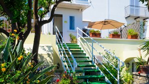 A staircase with green steps leading to a white building, surrounded by potted plants and flowers. - Albergo Villa Giusto (Barano d'Ischia)