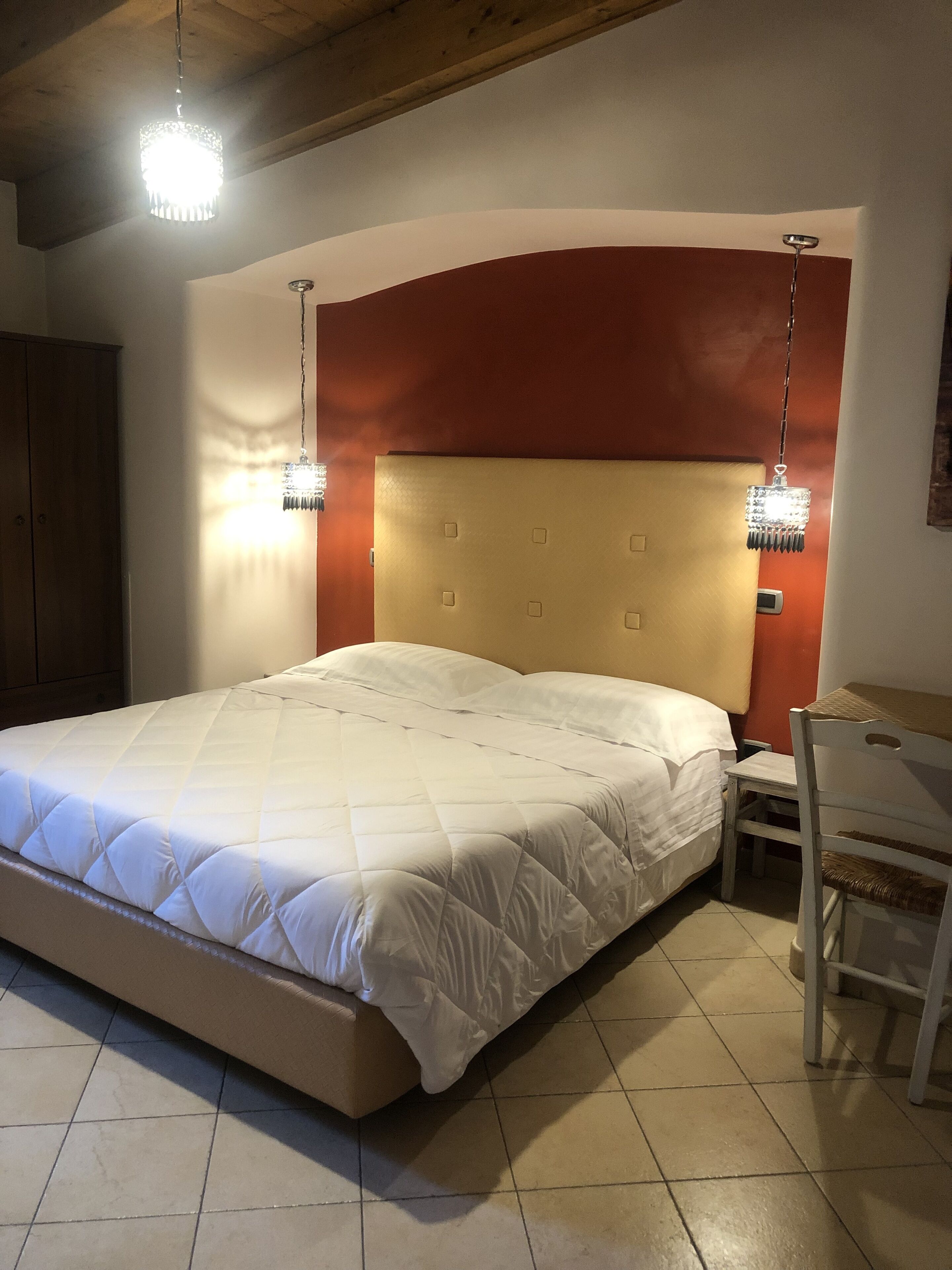 A bedroom with a large bed, a wooden desk, and two pendant lights.