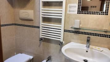 A bathroom with a toilet, bidet, and sink. There is a towel rack with folded towels, a glass shelf with toiletries, and a mirror with a chandelier.