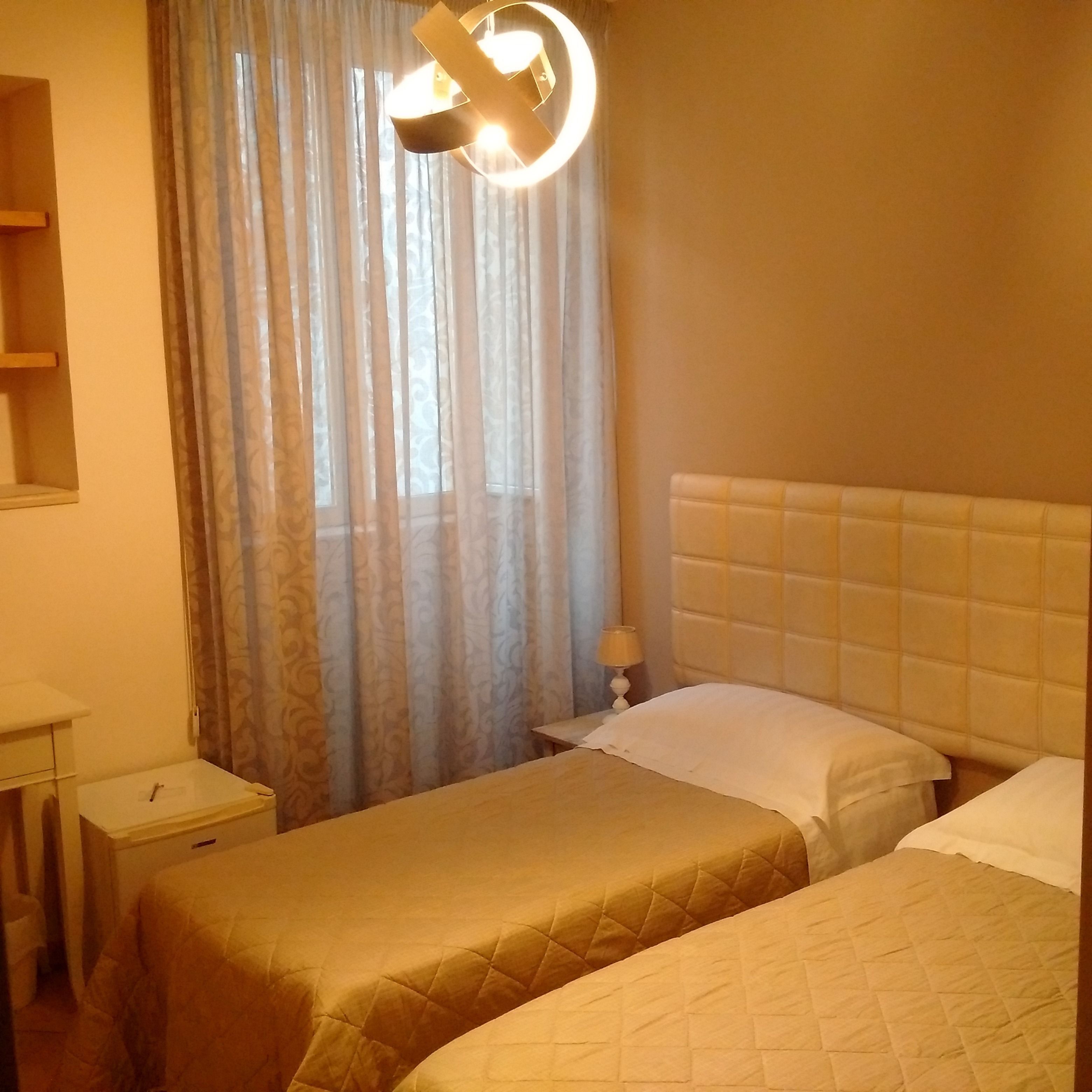 A hotel room with two beds, a bedside table, a lamp, and a window with curtains.