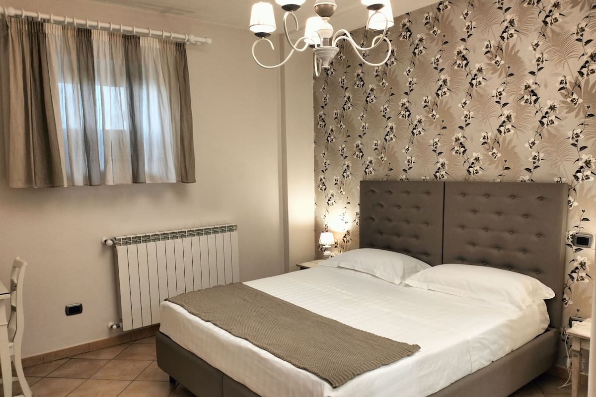 A bedroom with a large bed, a radiator, a chair, and a wall with floral wallpaper.