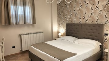 A bedroom with a large bed, a radiator, a chair, and a wall with floral wallpaper.