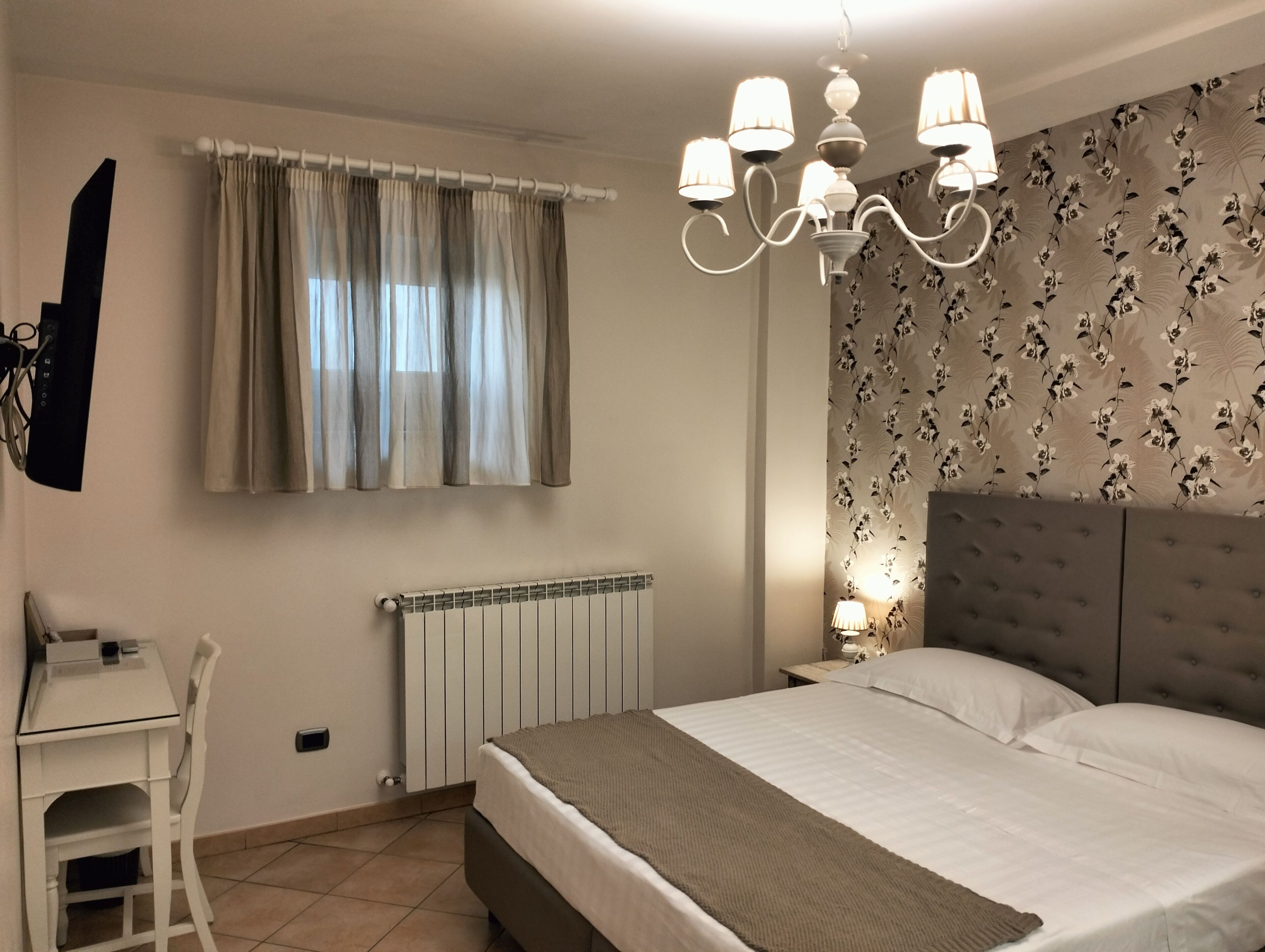 Un dormitorio con cama, escritorio, silla, radiador y ventana con cortinas.