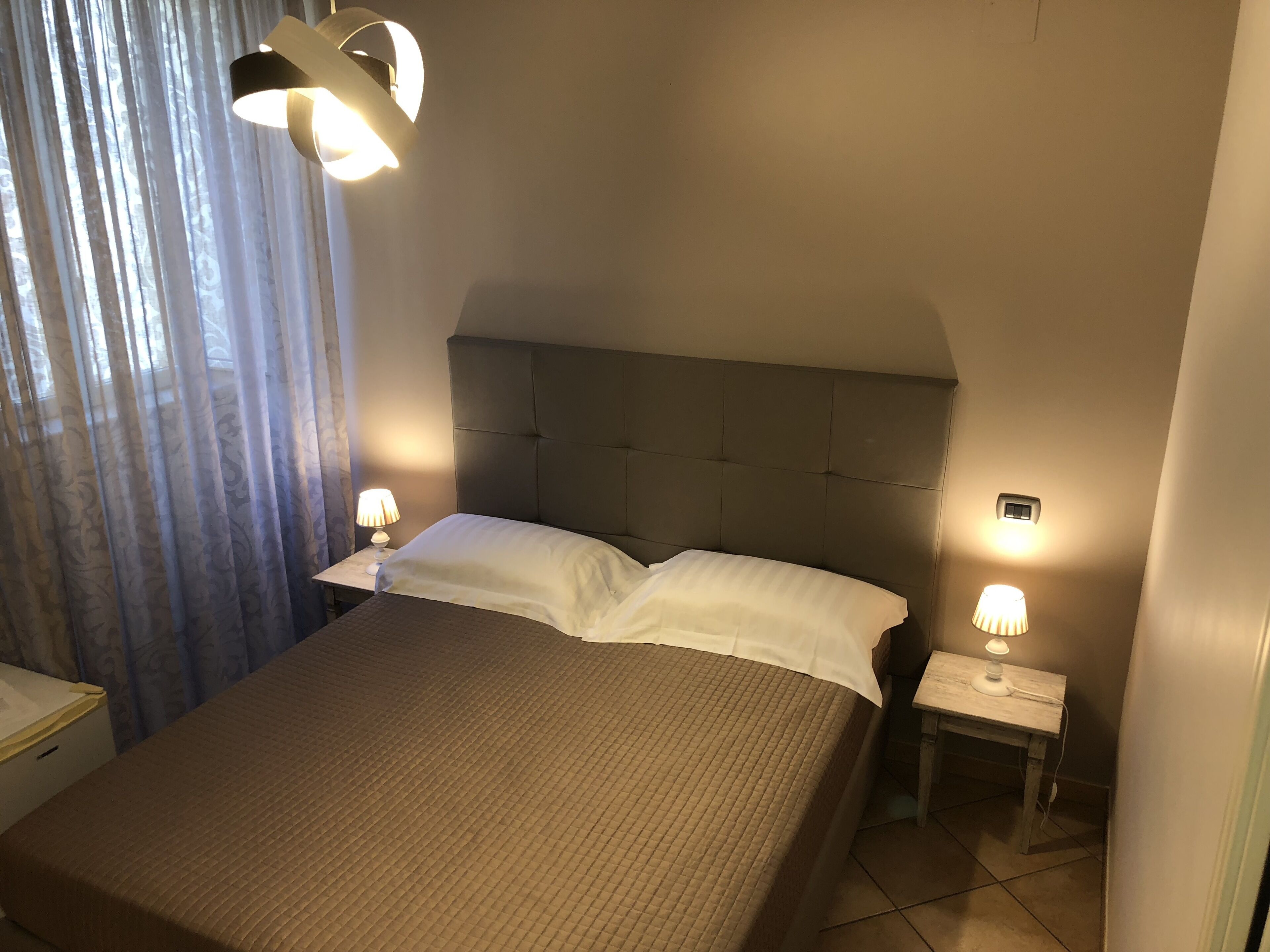 A neatly made bed with a headboard, two bedside tables with lamps, and a window with curtains.