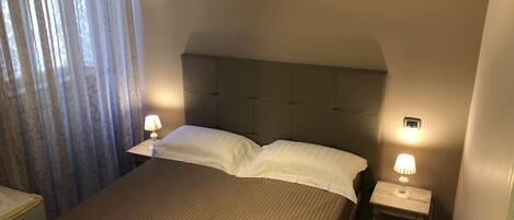 A neatly made bed with a headboard, two bedside tables with lamps, and a window with curtains.