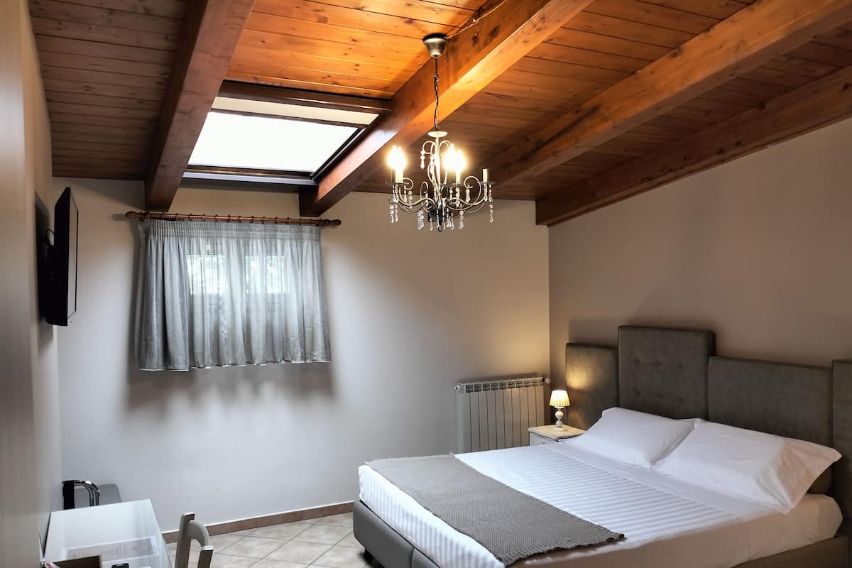 A bedroom with a bed, a desk, a chair, a chandelier, and a window with curtains.
