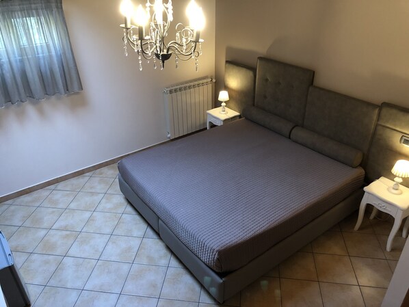 A bedroom with a large bed, a chandelier, a bedside table with a lamp, and a radiator. - Bed & Breakfast De Nittis - Meridia Collection (Barletta)