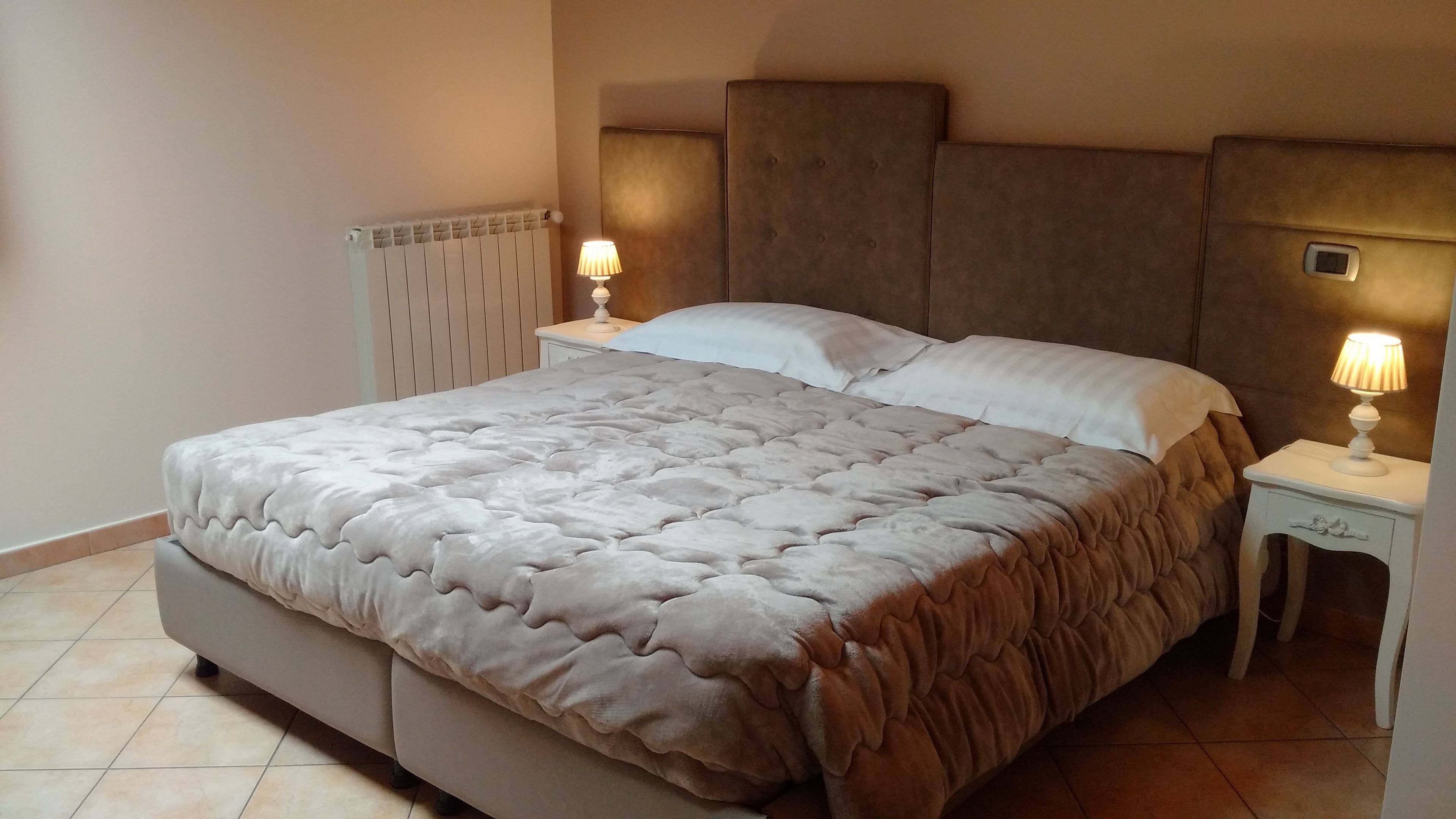 A bedroom with a large bed, two bedside tables with lamps, a headboard, and a radiator.