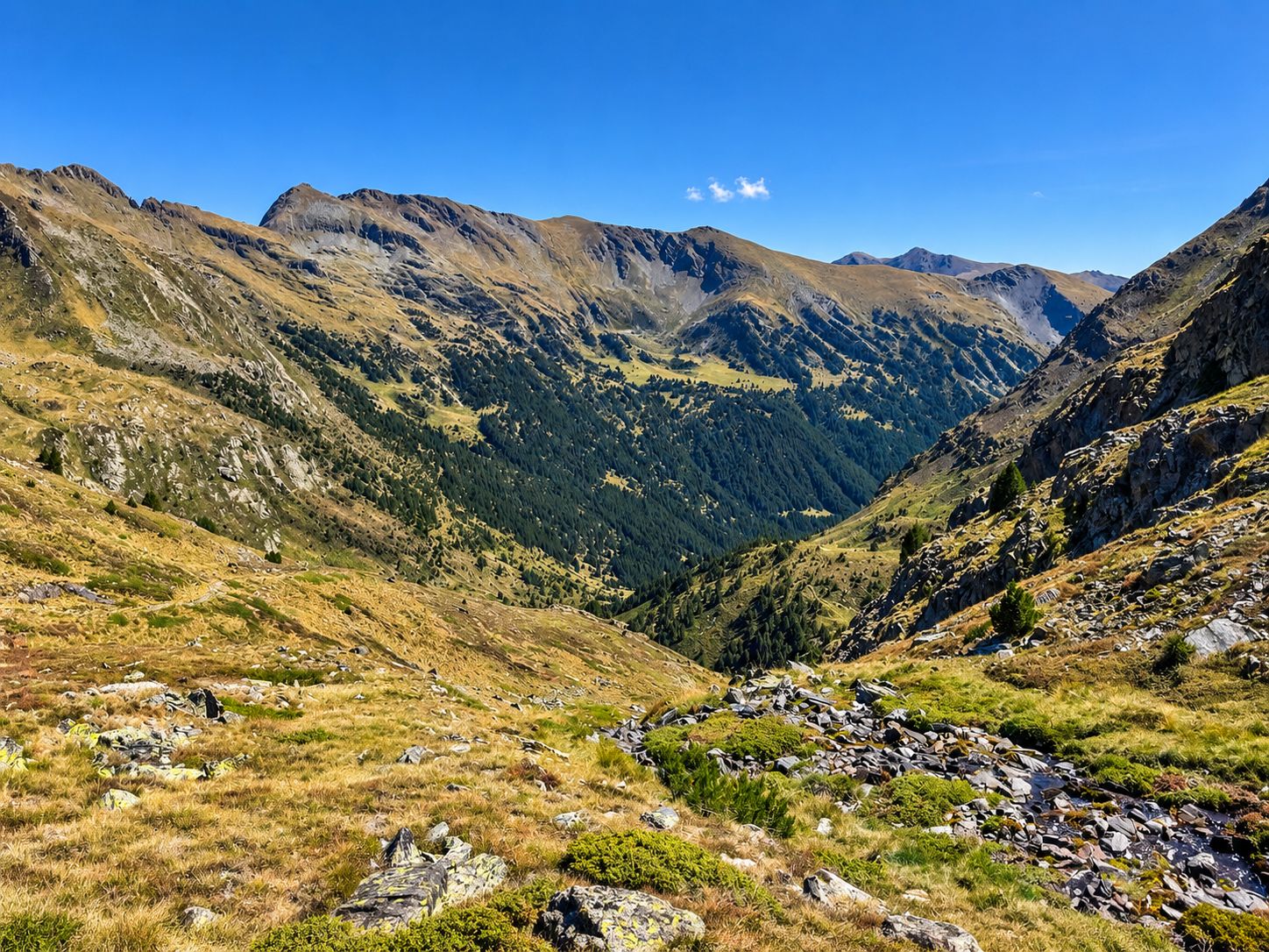 A mountainous landscape with a valley, rocky terrain, and sparse vegetation.