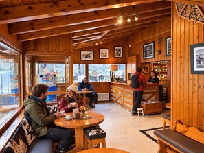 A wooden interior with a bar area, seating, and framed pictures on the walls. - Hotel Bruxelles (Soldeu)