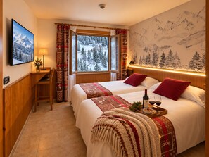 Habitación de hotel con una cama grande, una ventana con vistas a árboles cubiertos de nieve, un televisor montado en la pared y un escritorio de madera.