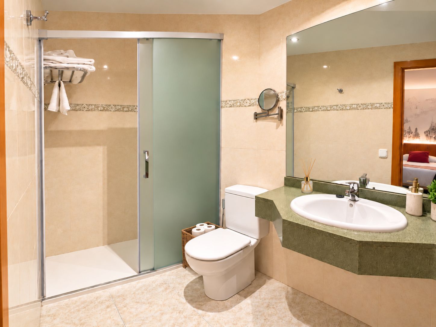 Un baño con cabina de ducha de vidrio, inodoro, lavabo con espejo y una pequeña cesta de mimbre con papel higiénico.