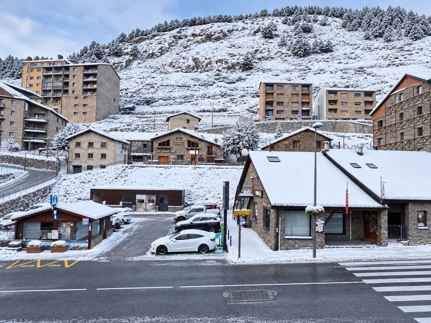 Un pueblo cubierto de nieve con edificios, una carretera y automóviles estacionados.