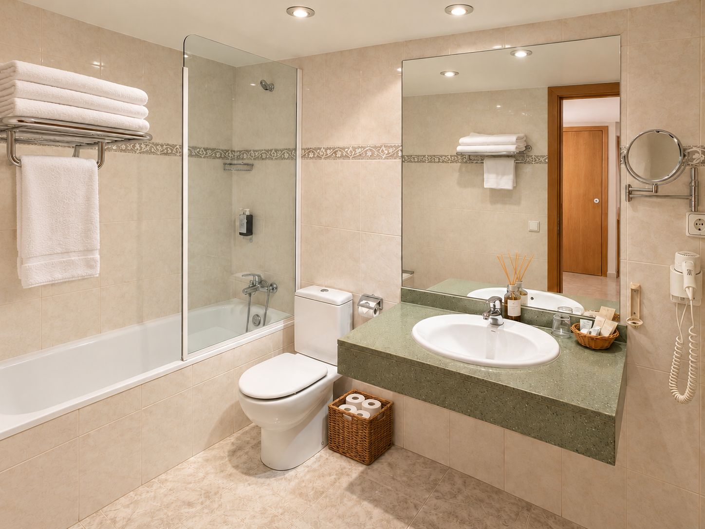 Un baño moderno con ducha de vidrio, inodoro blanco, lavabo con espejo y una cesta de artículos de aseo.