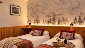 Habitación de hotel con dos camas, cabeceros de madera, un mural de montañas y una mesita de noche con una bandeja de alimentos para el desayuno.