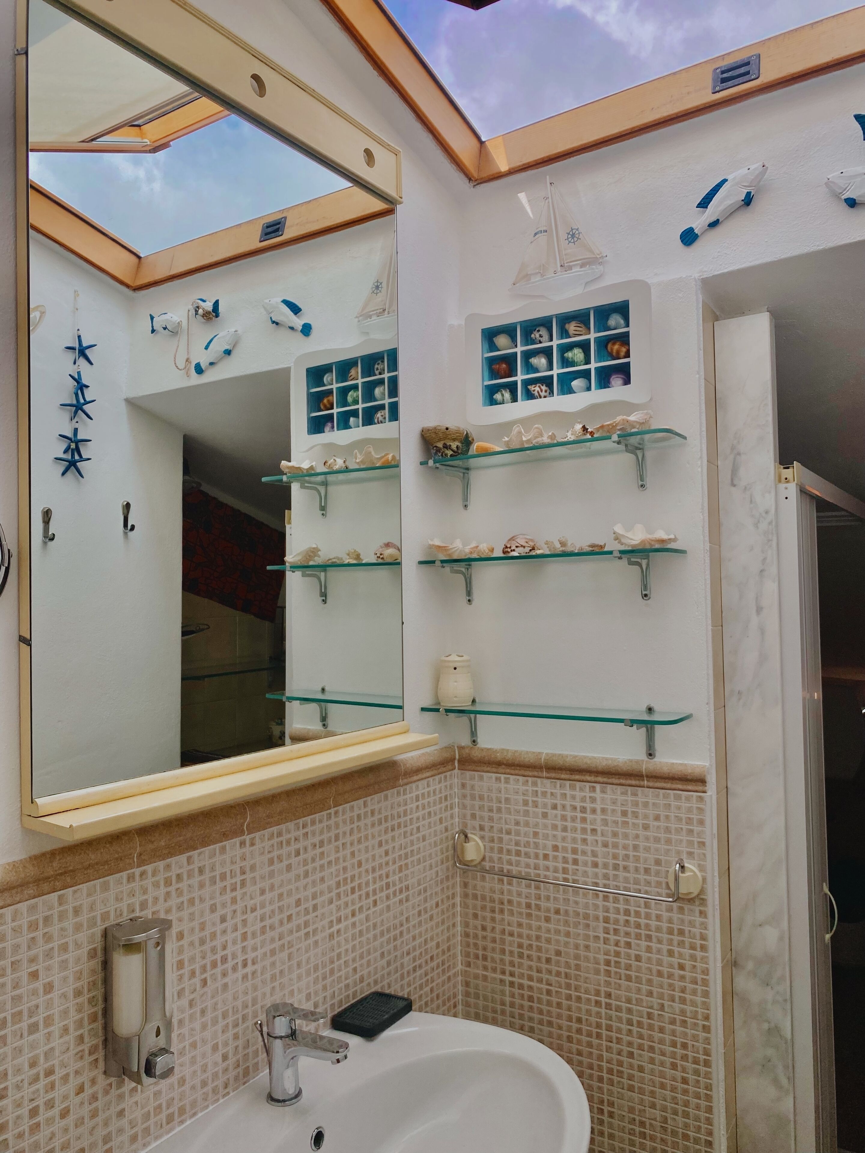 Een badkamer met dakraam, grote spiegel en planken met decoratieve objecten.