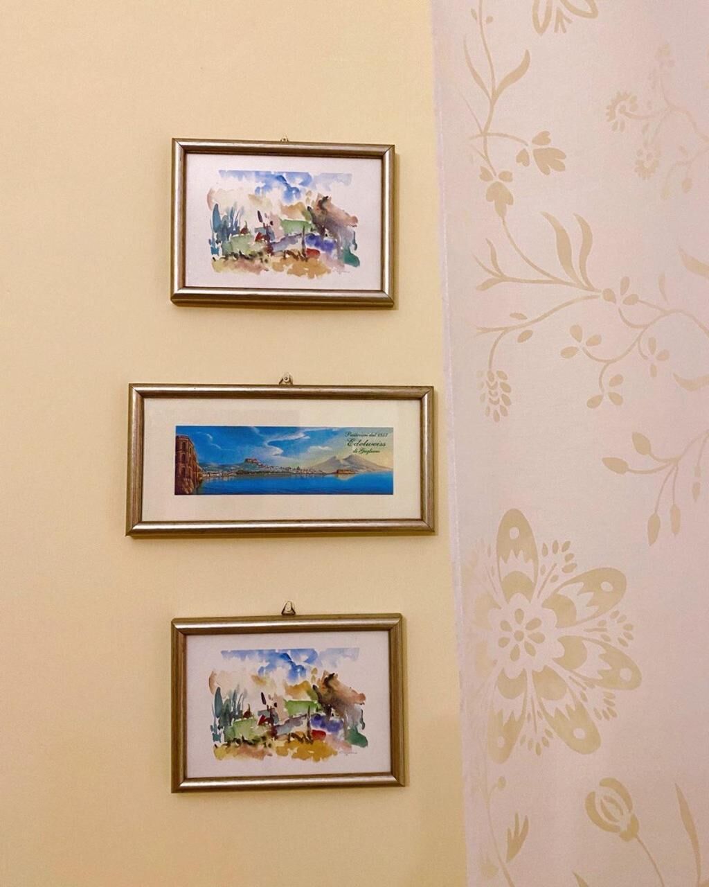 Three framed artworks on a wall with a floral wallpaper pattern.
