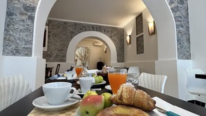 A breakfast setting with a table, plates of fruit, croissants, and a glass of orange juice. - Al Vecchio Pioppo (Praia a Mare)