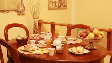 Una mesa de comedor lista con productos para el desayuno, como pan, bollería, fruta y bebidas.