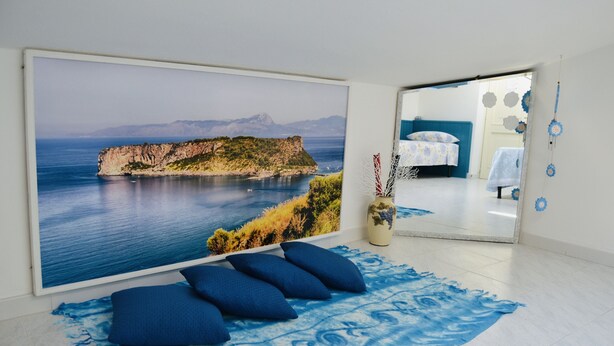 A room with a large scenic wall mural, a bed with a blue headboard, and a blue patterned rug. - Al Vecchio Pioppo (Praia a Mare)