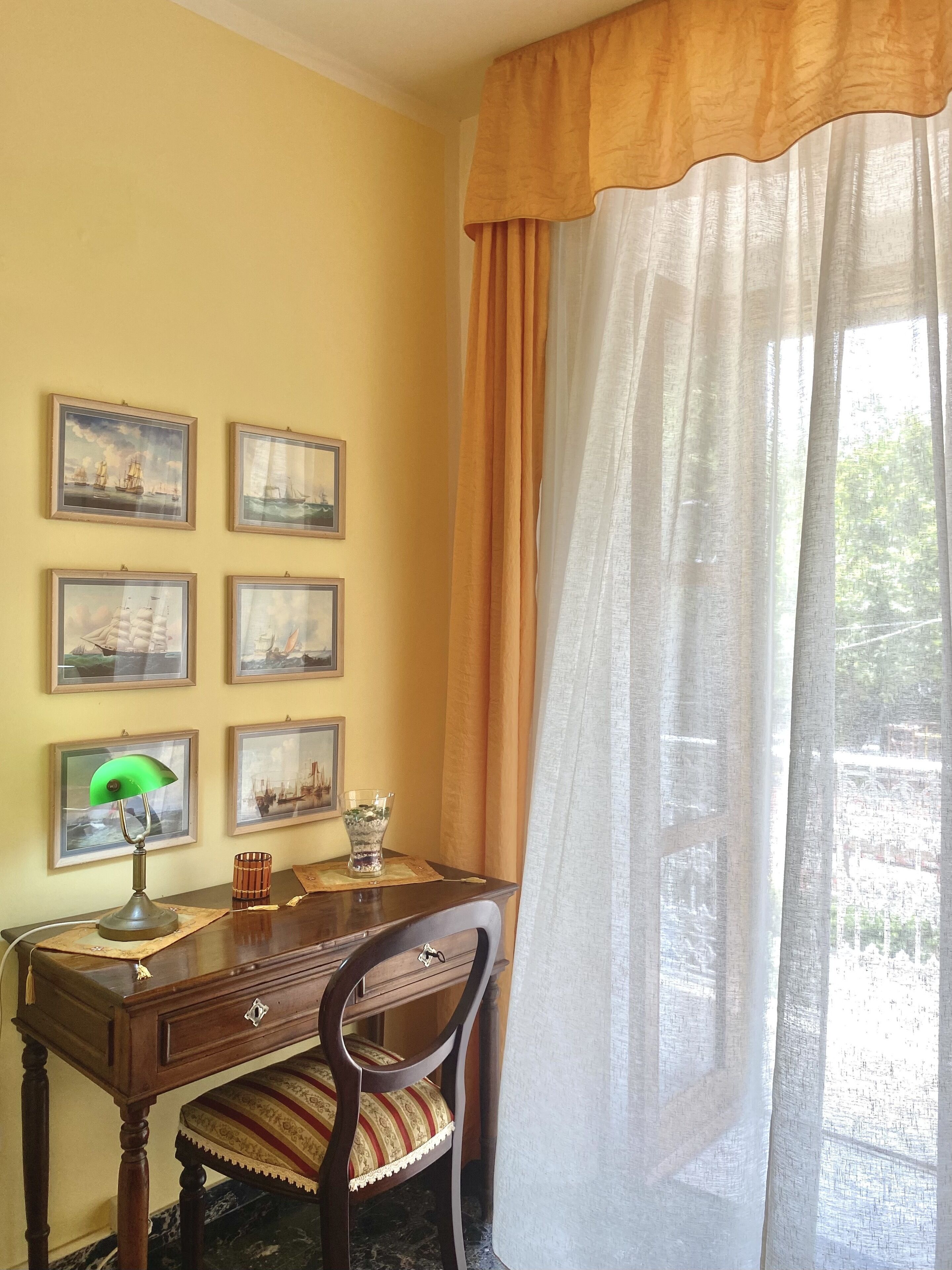 Una habitación con un escritorio de madera, una silla, una lámpara y cuadros enmarcados en la pared.