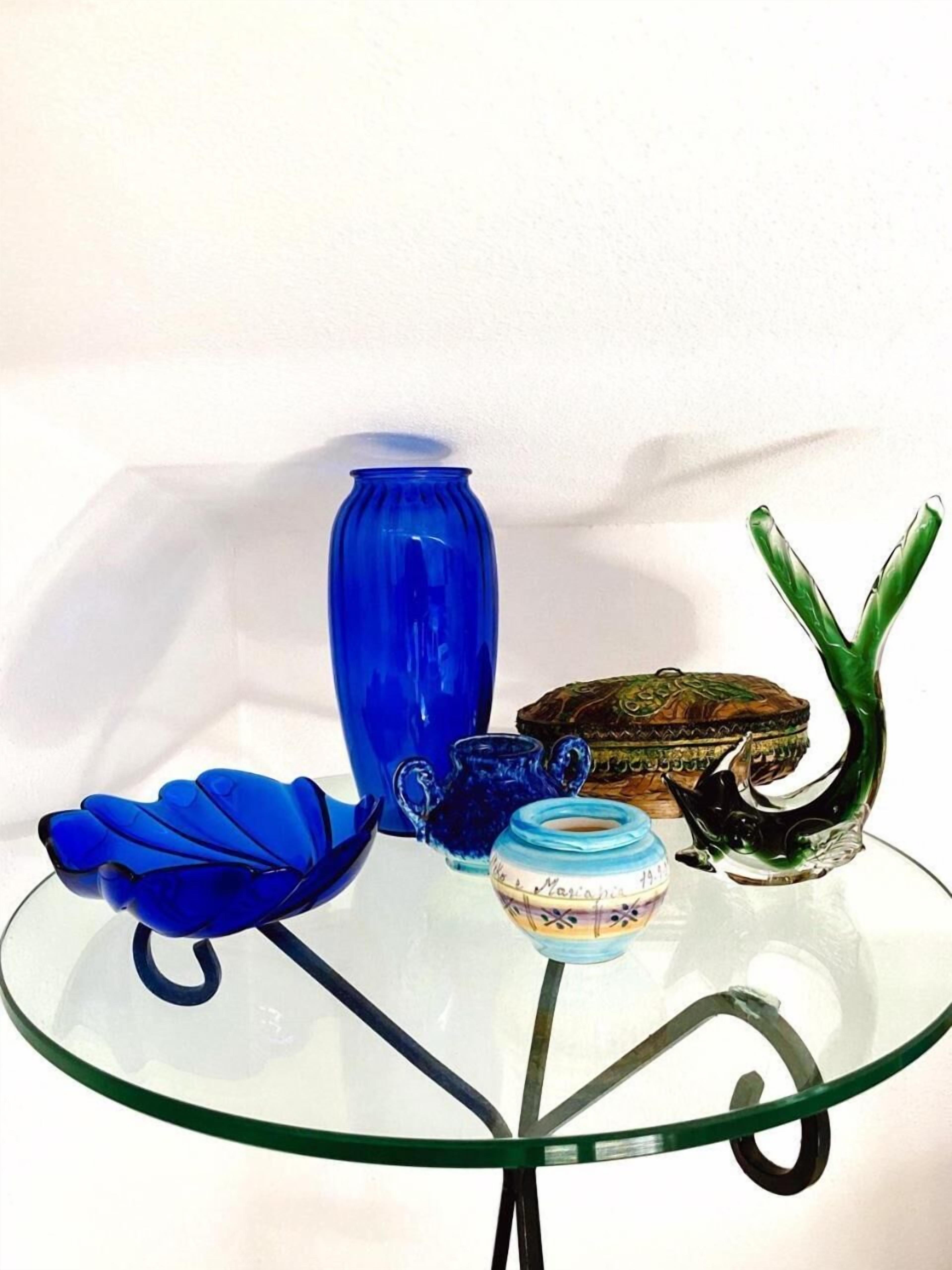 A glass table with various glass objects including a blue vase, a blue bowl, a green glass sculpture, and a small blue and white jar.