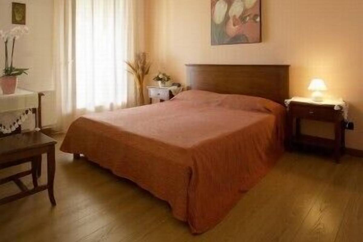 A bedroom with a wooden bed, a bedside table with a lamp, and a chair.