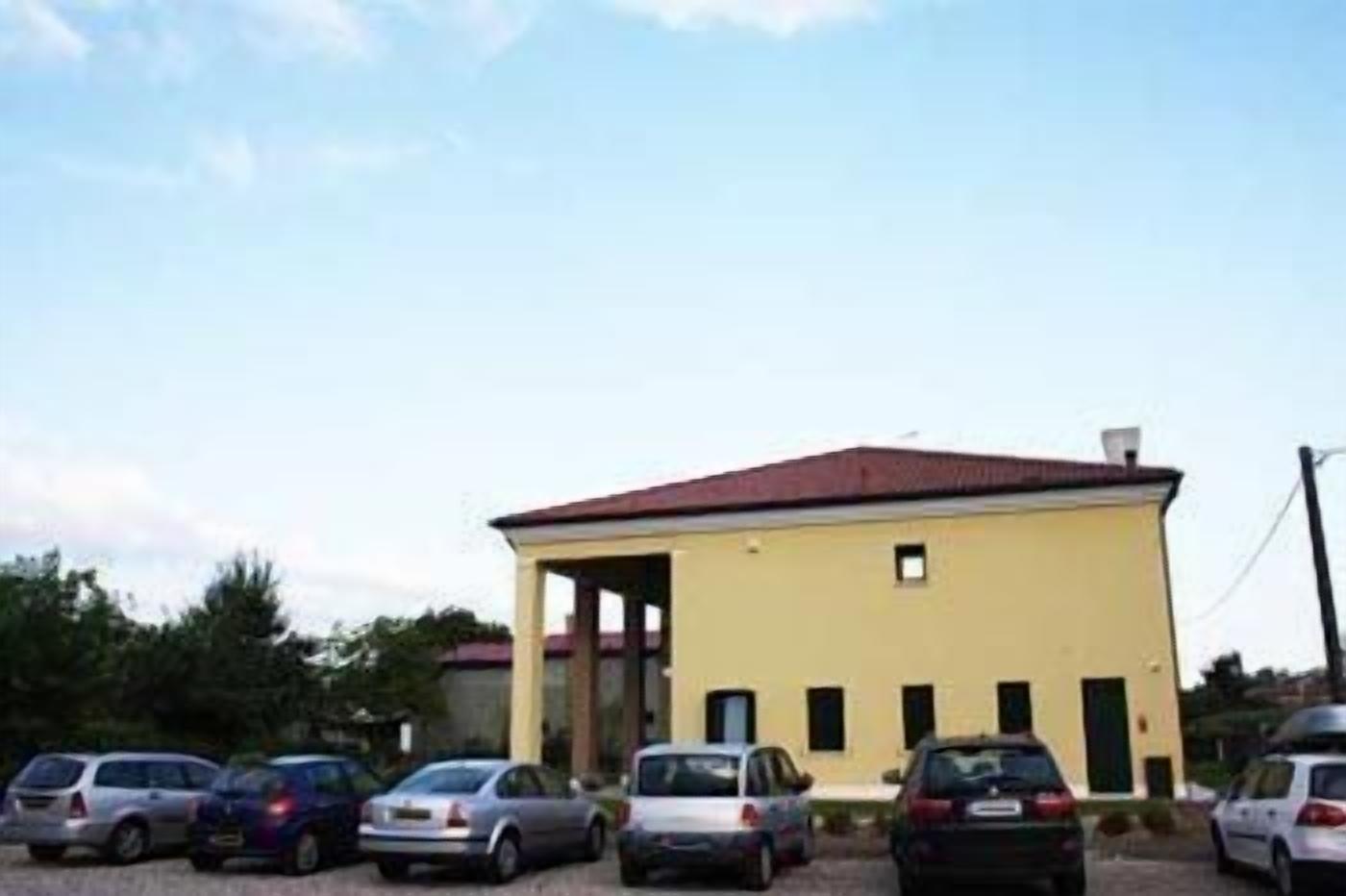 A single-story building with a flat roof and a small balcony. There are several cars parked in front.
