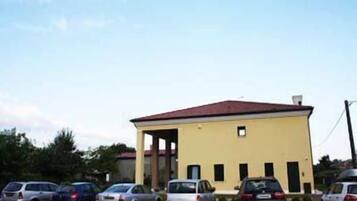 A single-story building with a flat roof and a small balcony. There are several cars parked in front.