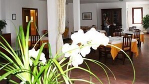 A dining area with tables set for meals, a large plant in the foreground, and a person standing near the back. - Ca' Florian (Zero Branco)