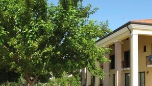 A building with a covered outdoor seating area, a tree, and a paved walkway. - Ca' Florian (Zero Branco)