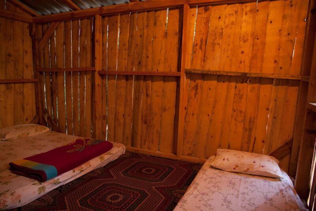 Una habitación de madera con dos camas, cada una con una colcha estampada y una manta roja sobre una de ellas.